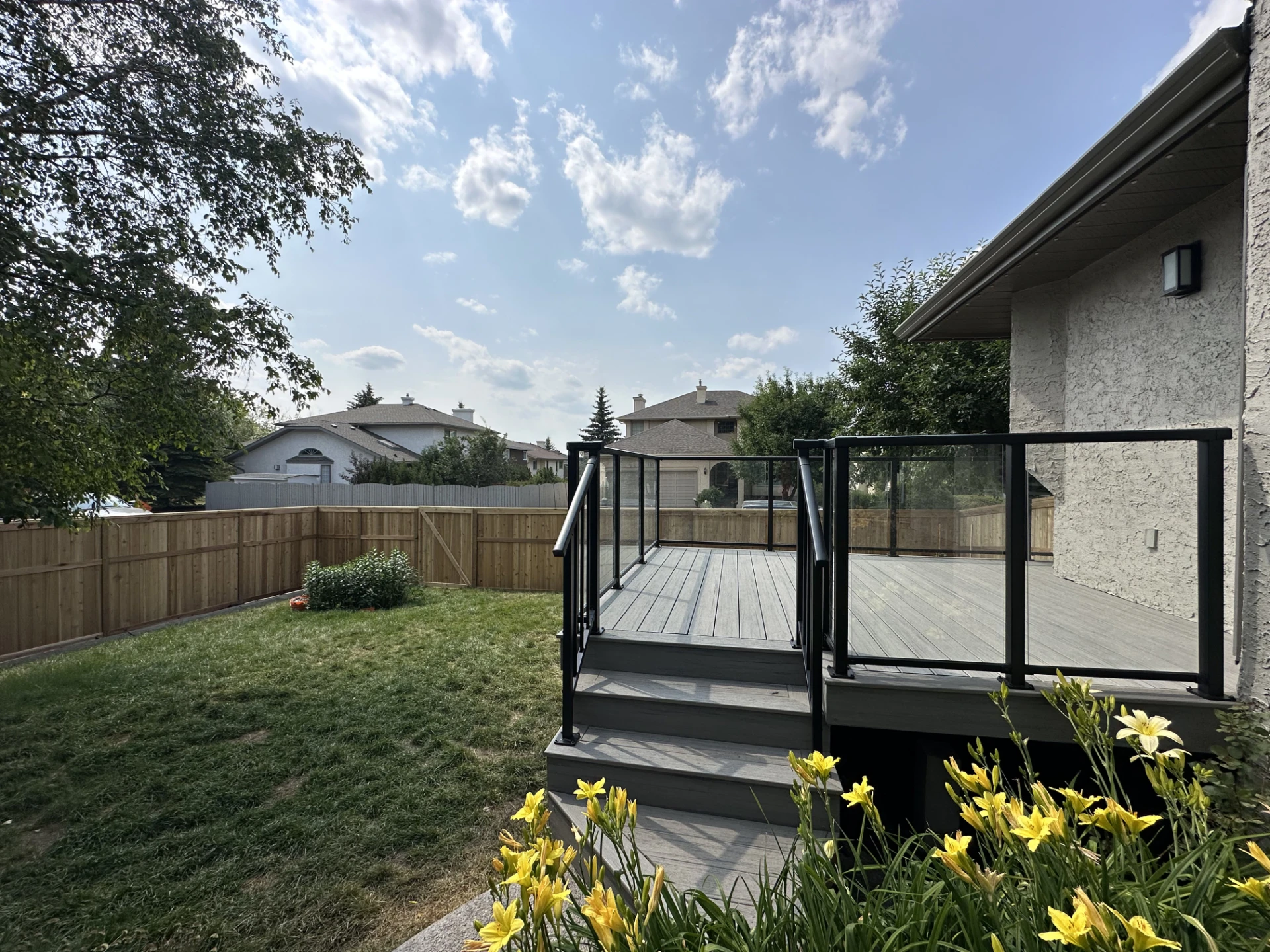 Backyard view of composite deck, stairs, and fenced lawn.