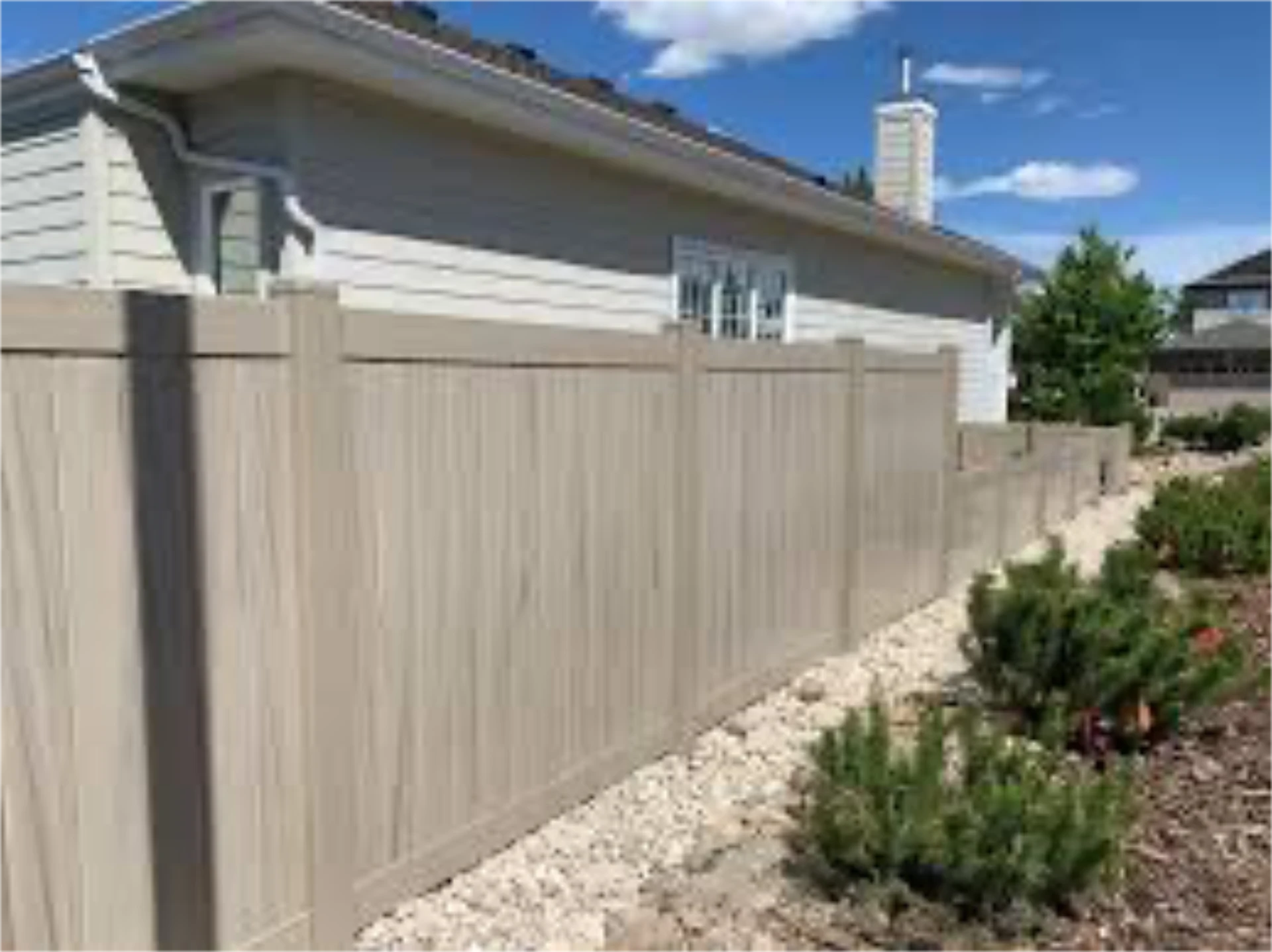 Beige vinyl fence beside landscaped rock garden.