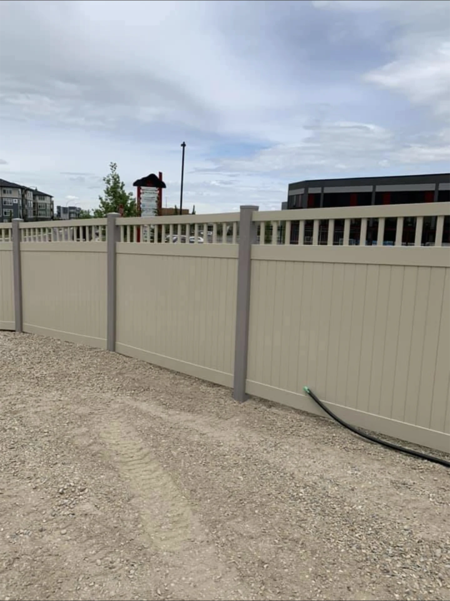 Beige vinyl privacy fence with decorative top rail.