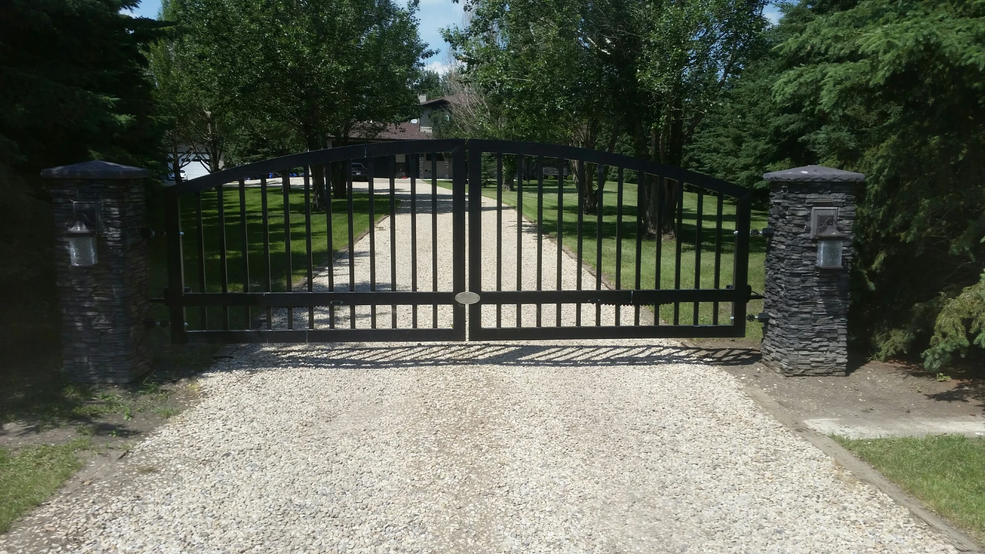 Black arched driveway gate between stone pillars