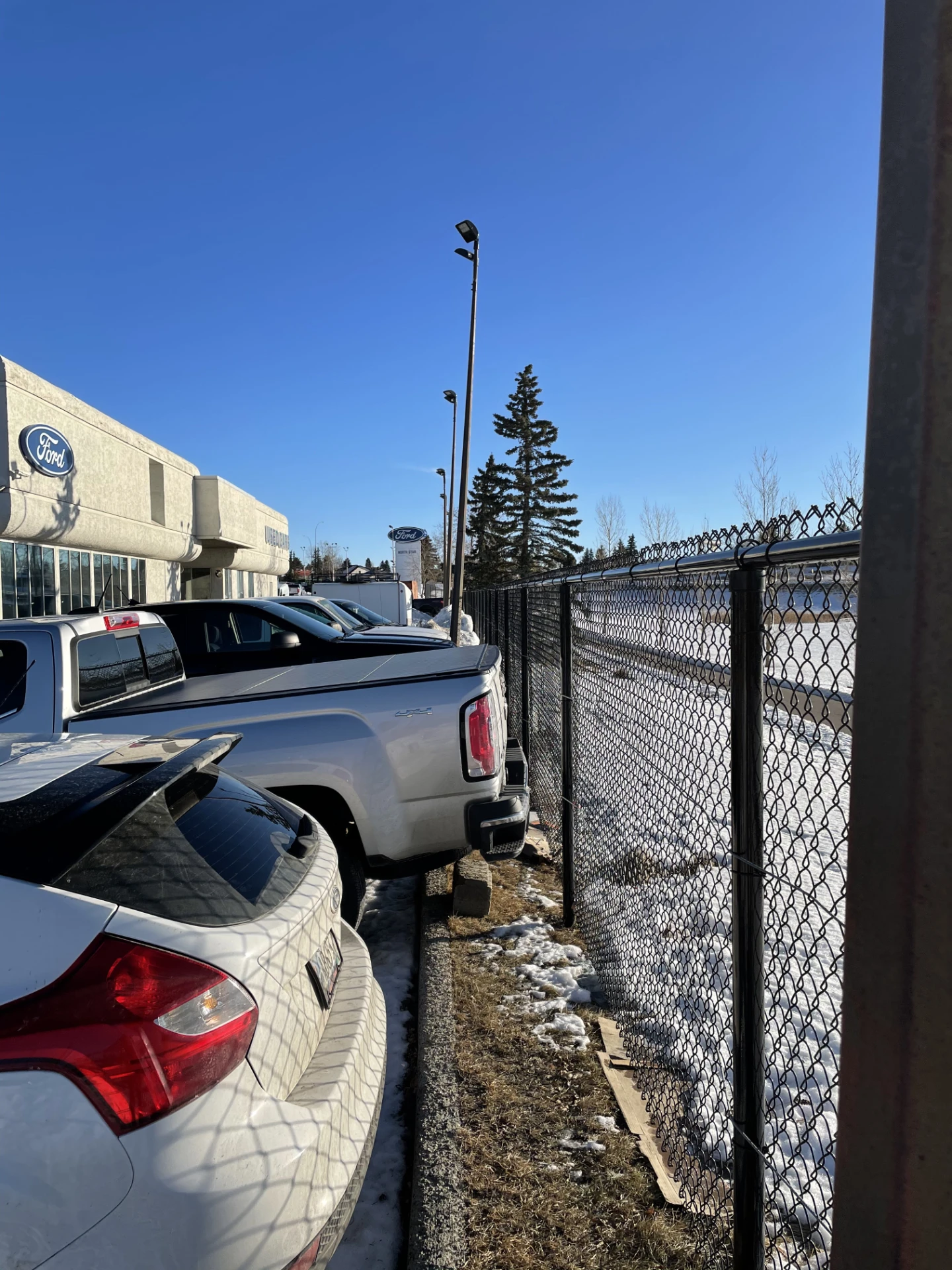 Chain link fence beside parked vehicles and snowy lot.