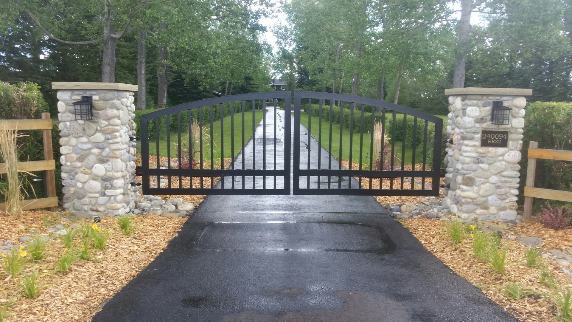 Double swing metal gate with stone columns and trees behind it