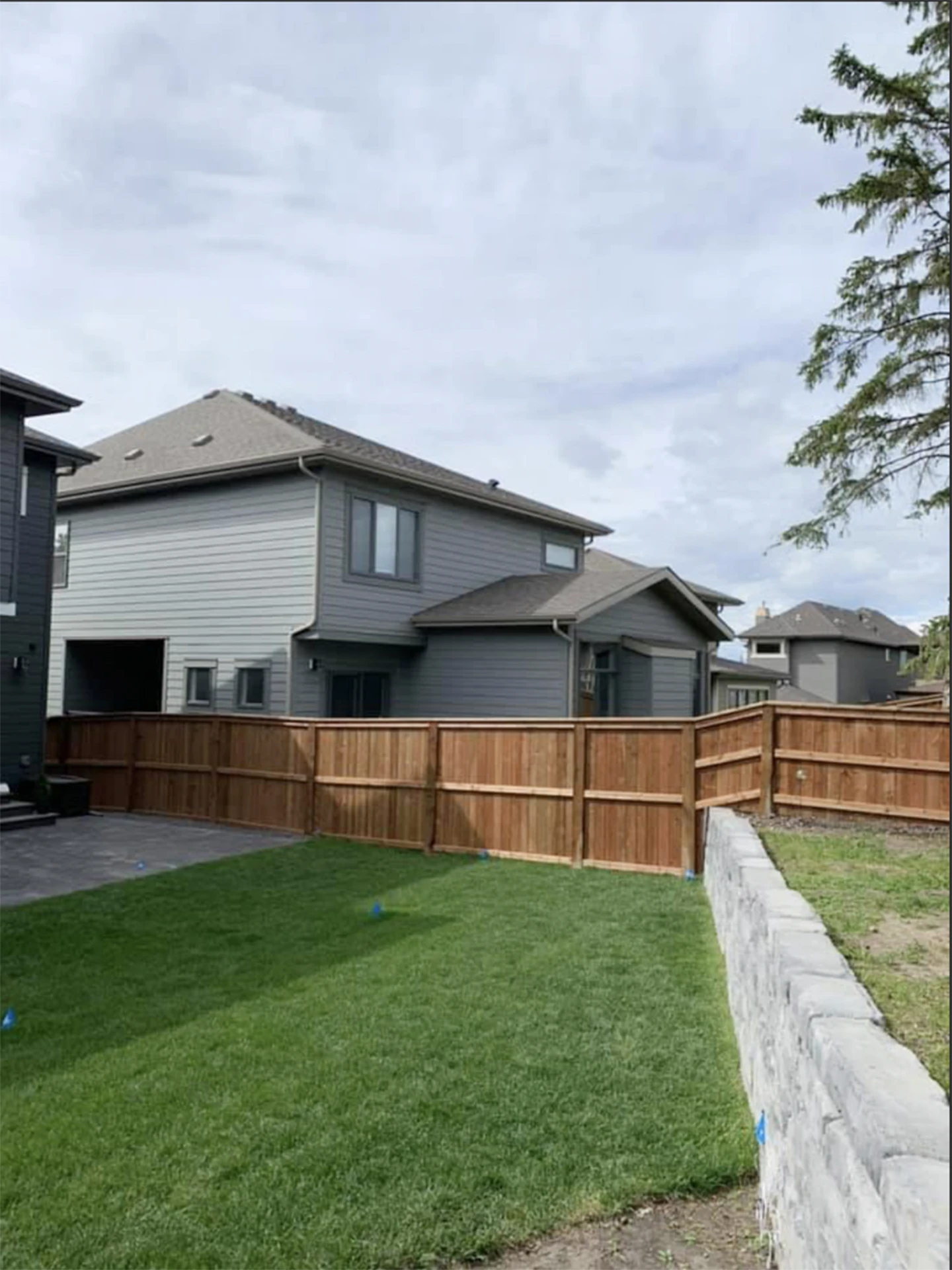 Fenced backyard with green lawn, retaining wall, and neighboring houses.