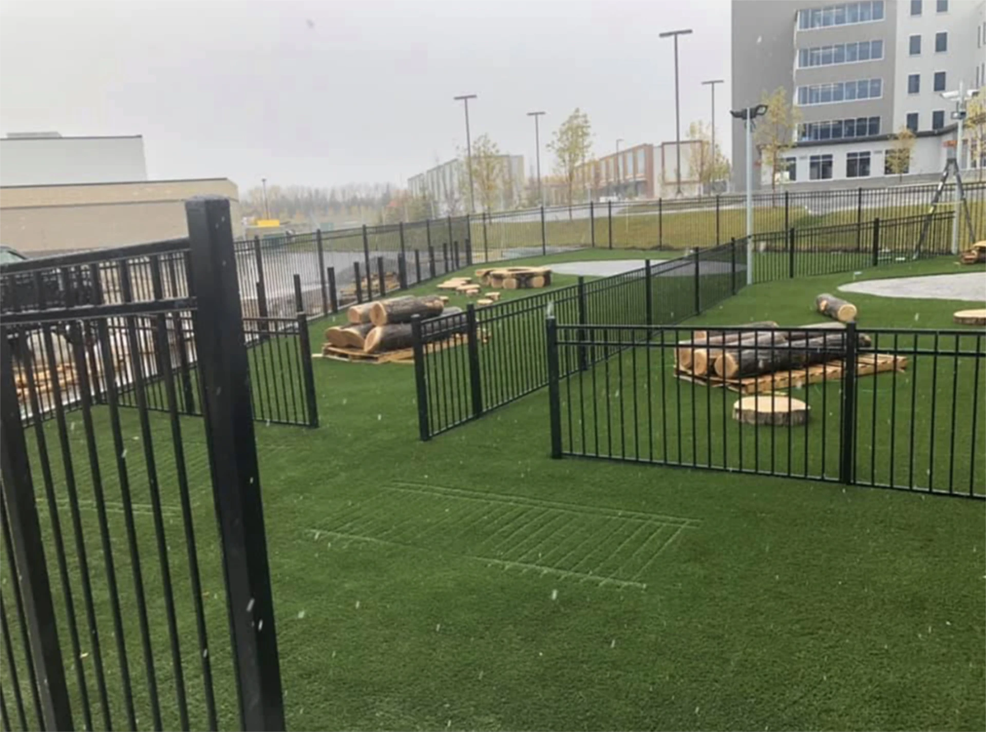 Fenced outdoor play area with artificial turf and log seating.
