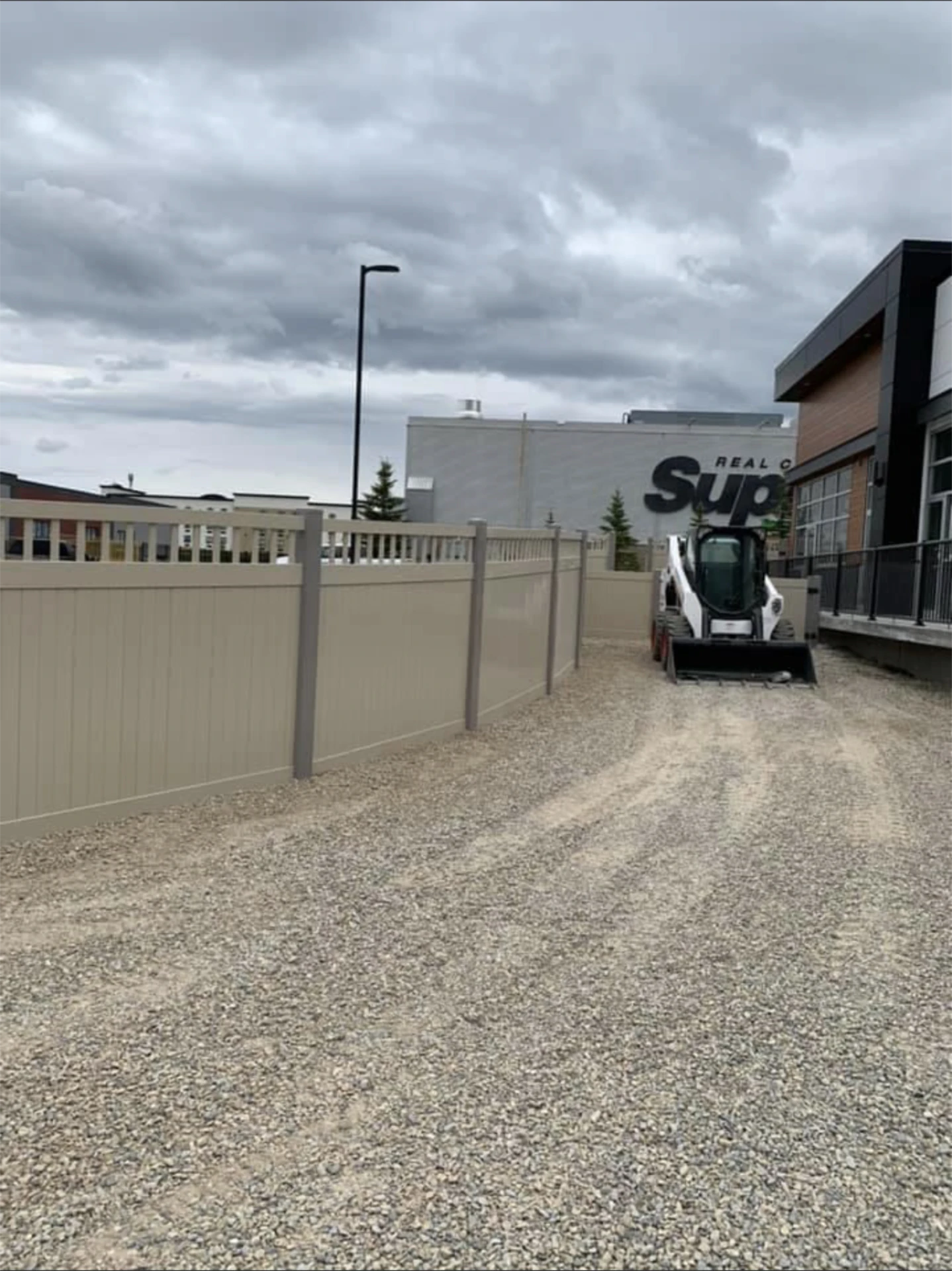 Long beige vinyl fence along a gravel driveway.
