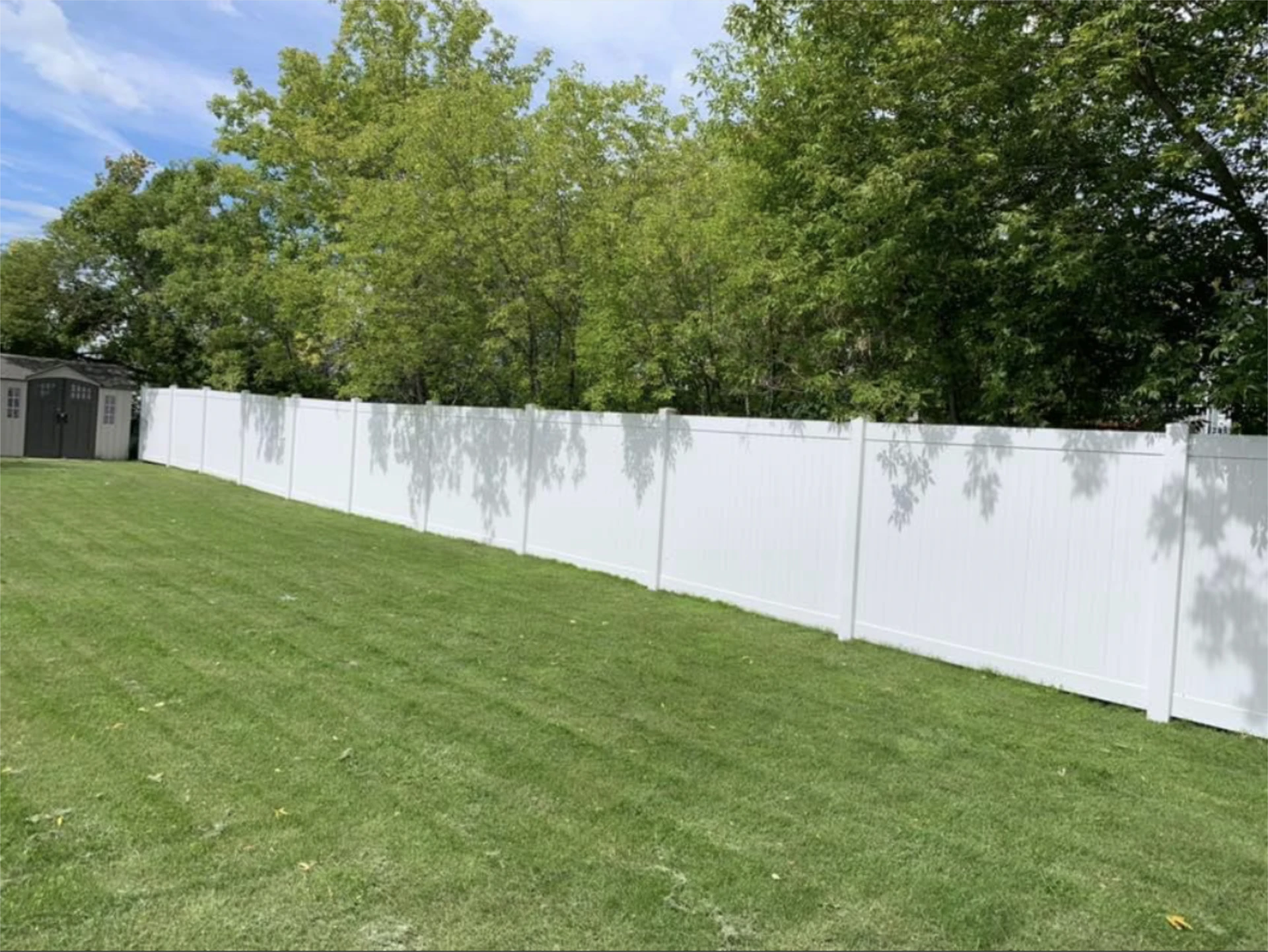 Long white vinyl privacy fence beside green lawn.