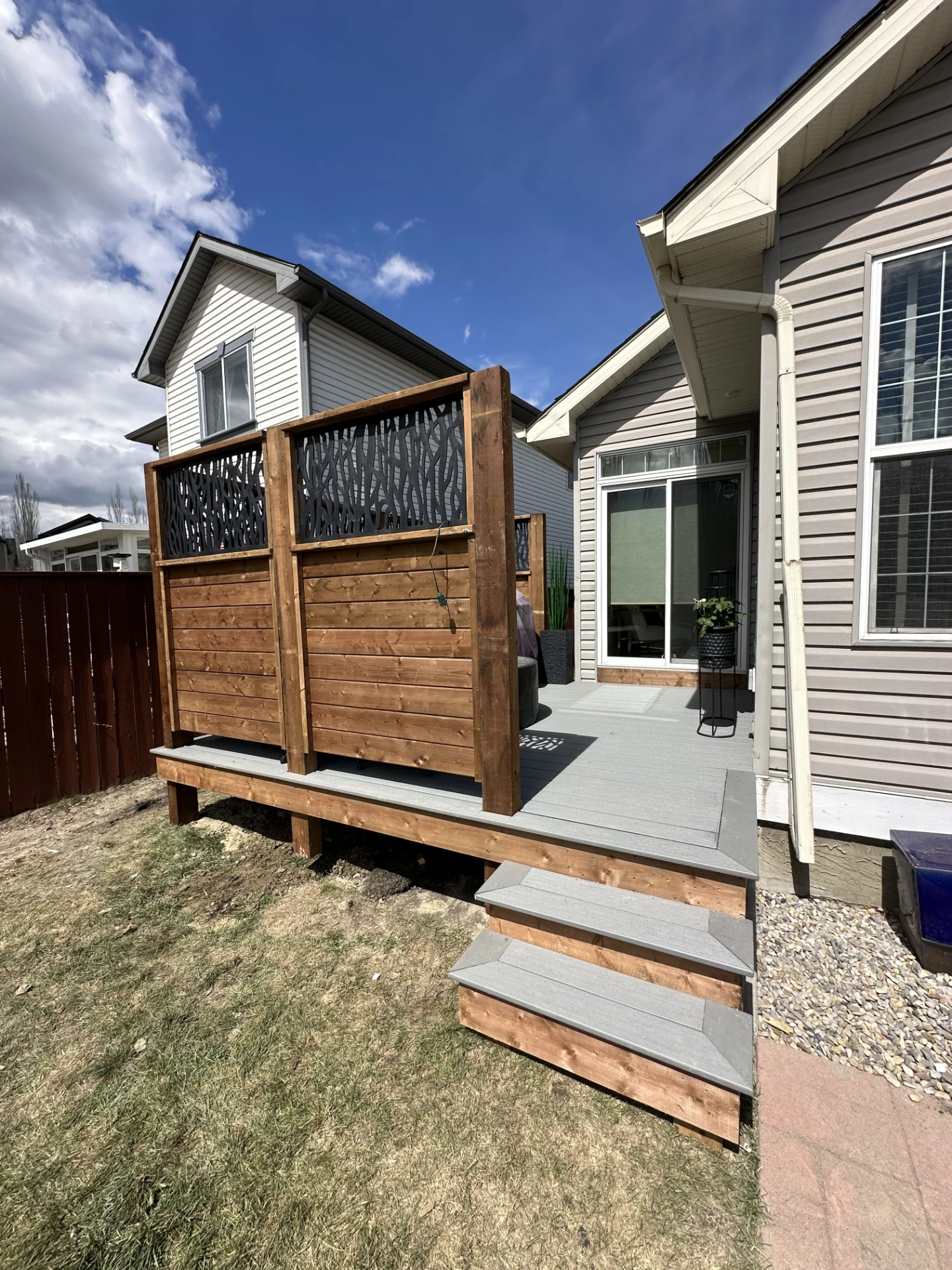 Raised backyard deck with decorative privacy panels and entry steps.
