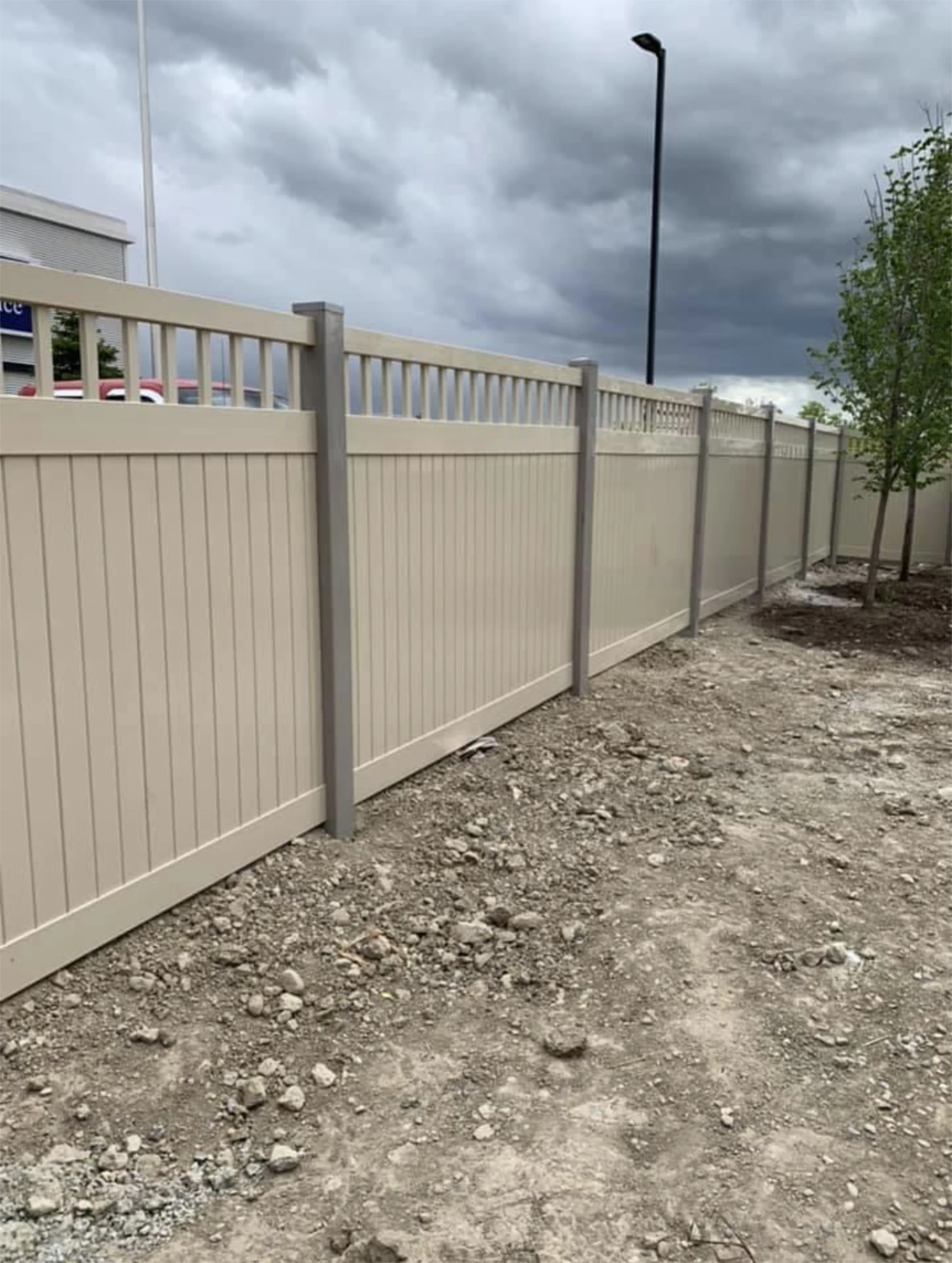 Tan vinyl fence with gray posts beside a gravel path.