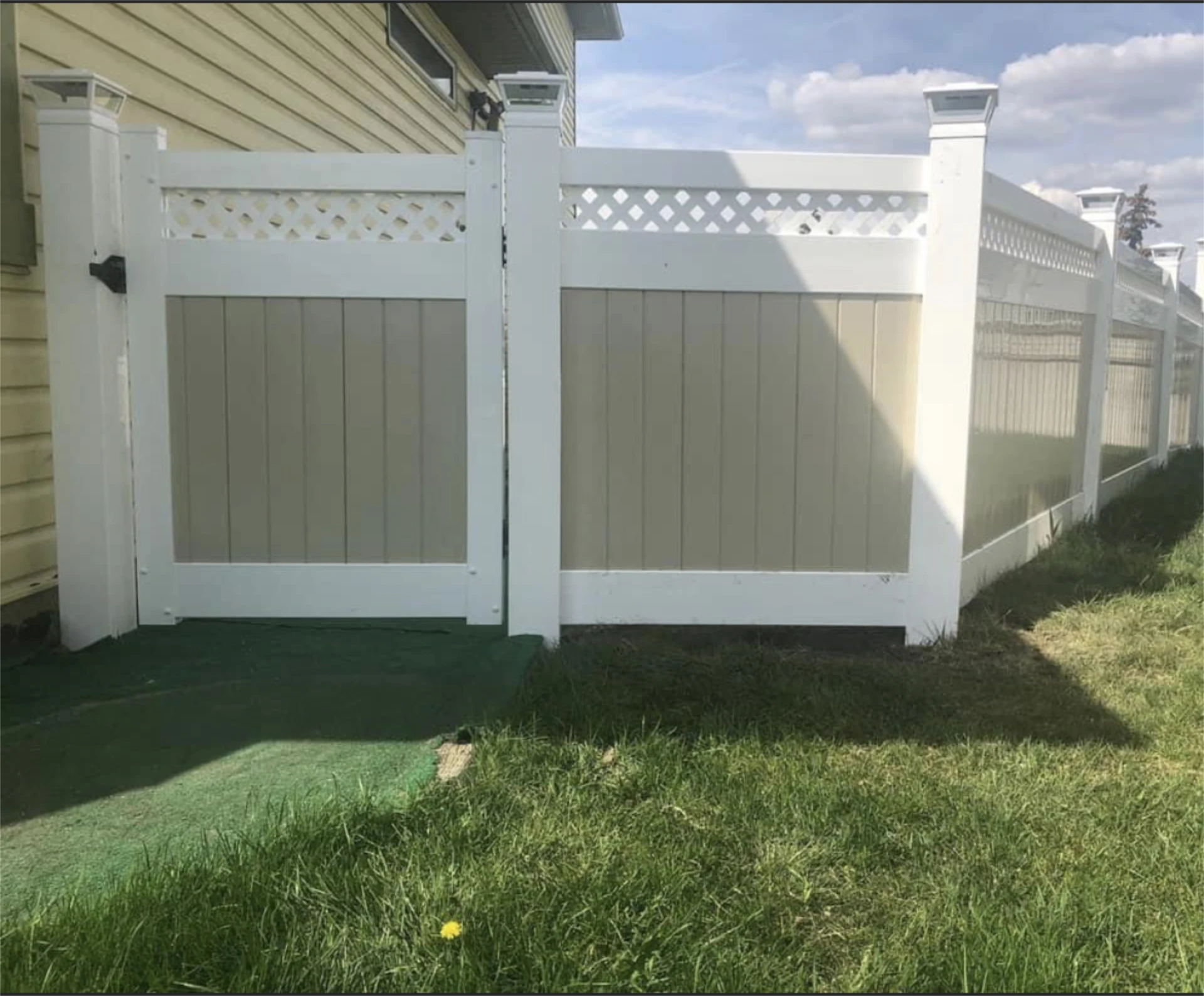 White vinyl privacy fence with gate beside house.