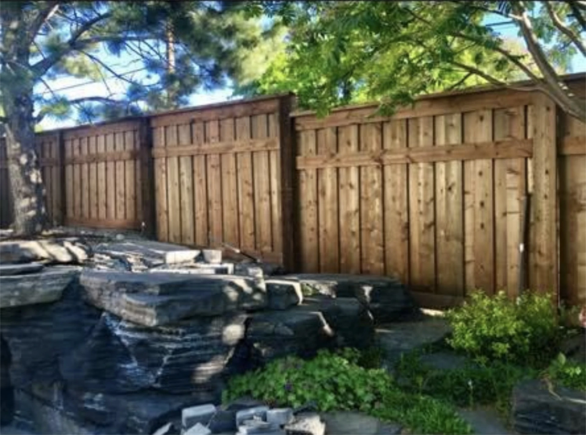 Wood fence behind pond and rocks.