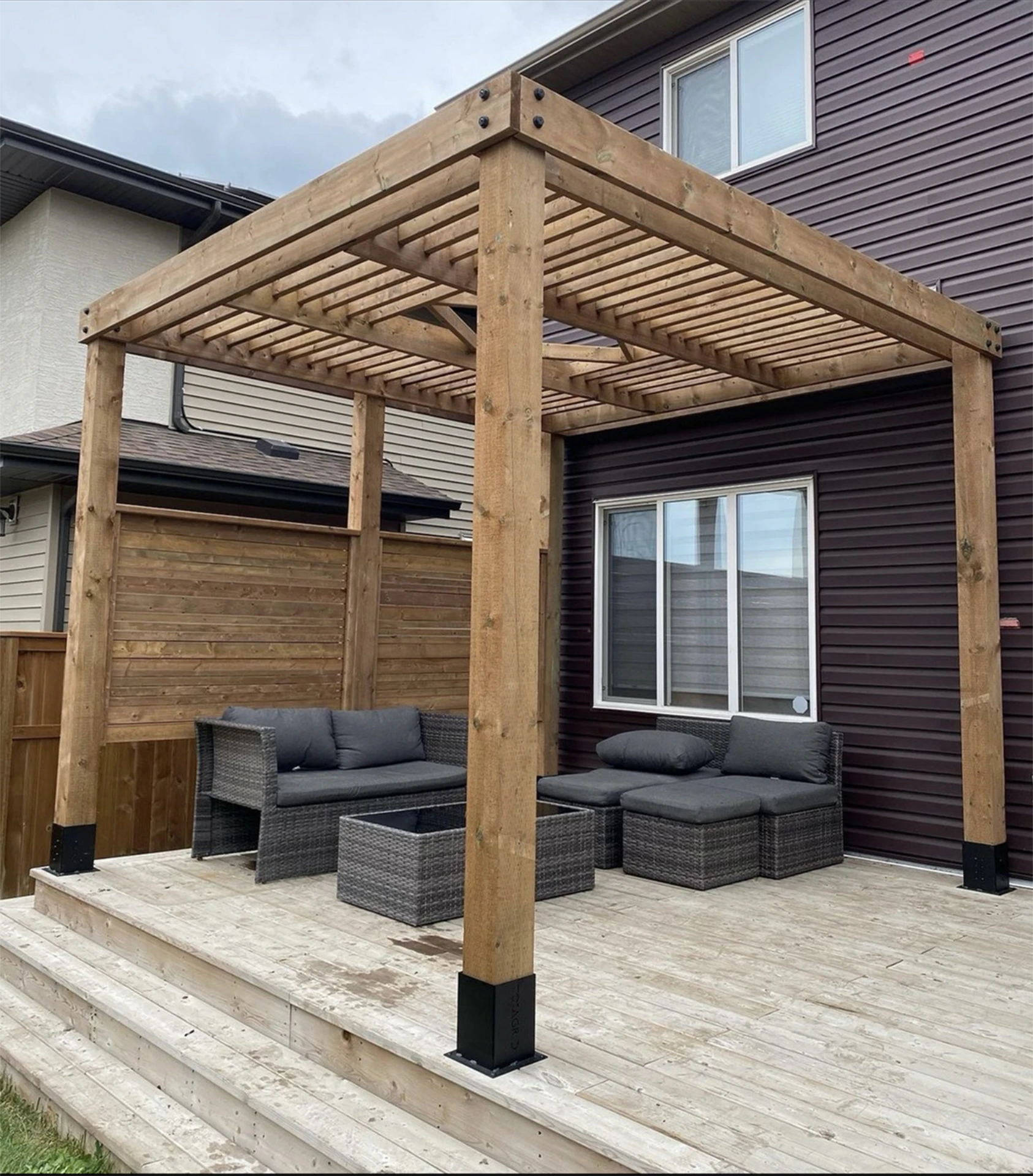 Wooden pergola over backyard deck seating area.