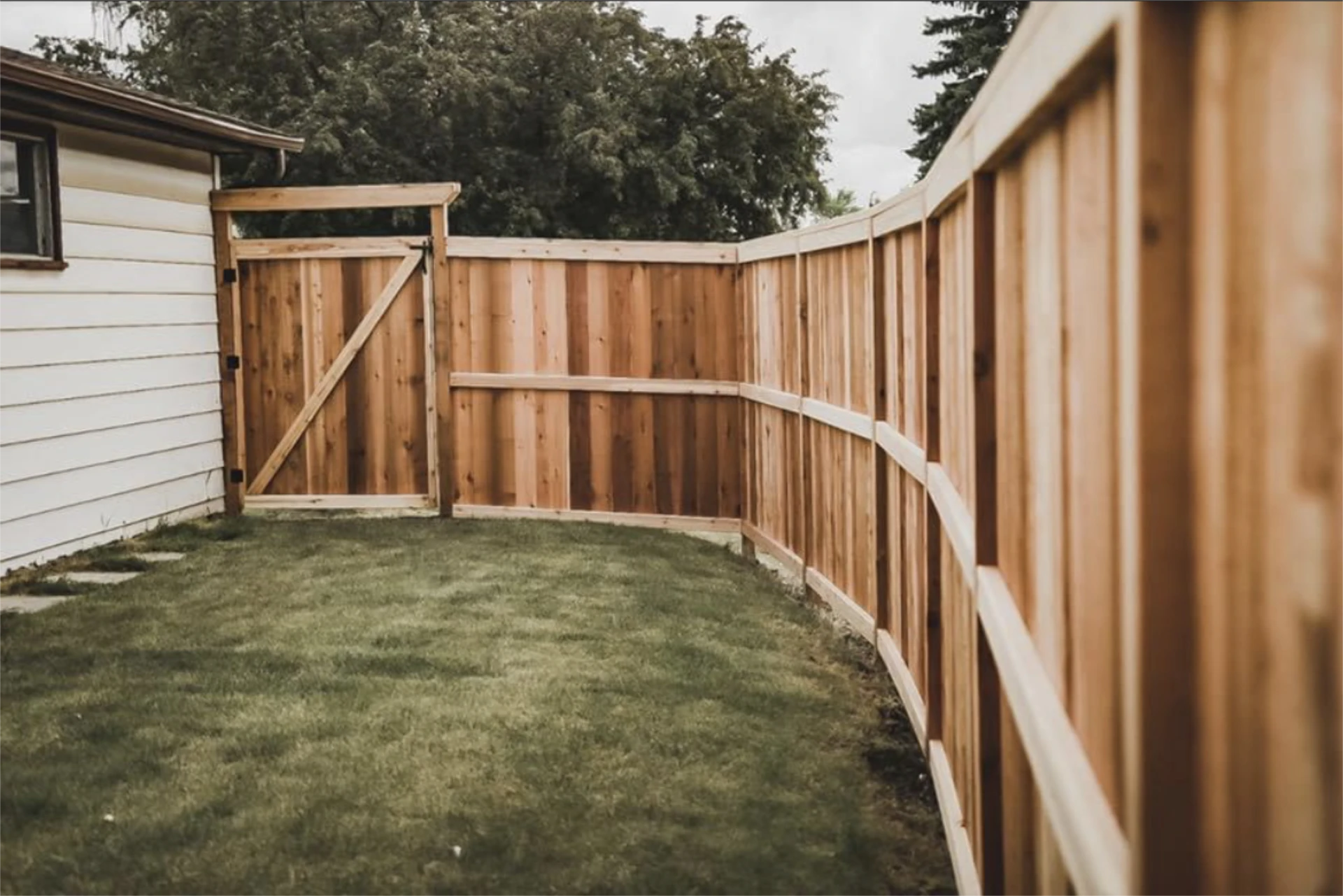 Wooden privacy fence and gate beside a grassy yard.