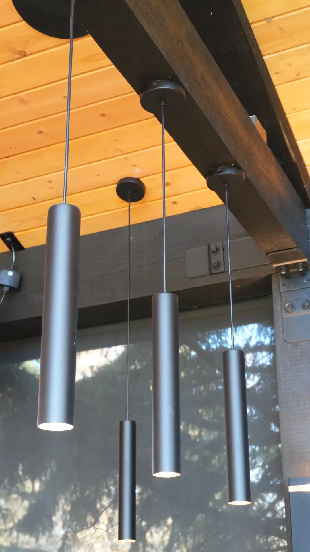 Black cylinder pendant lights under a cedar ceiling on a covered deck in Calgary, AB