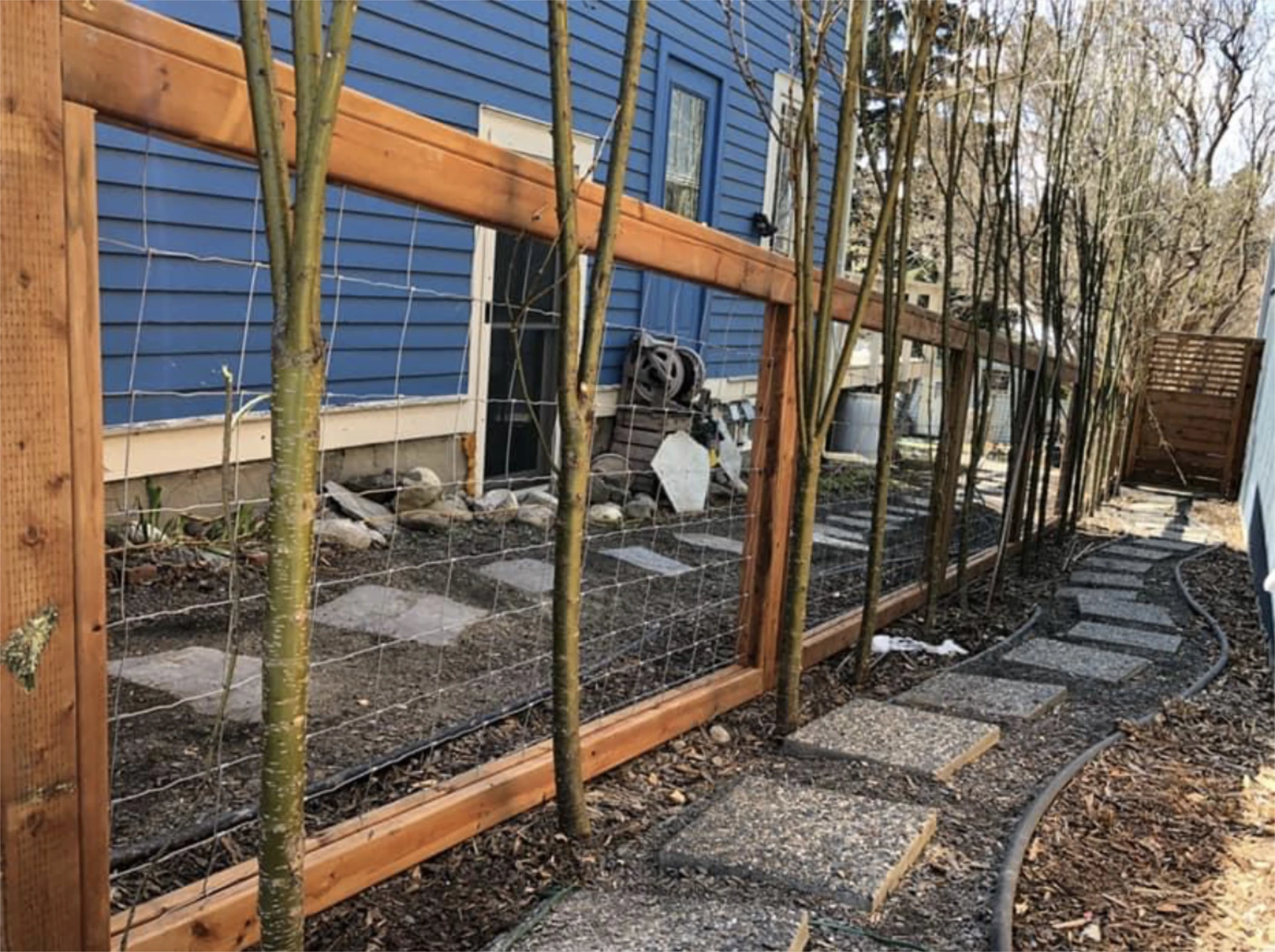 Curved stepping stone path along wood and wire long fence with trees