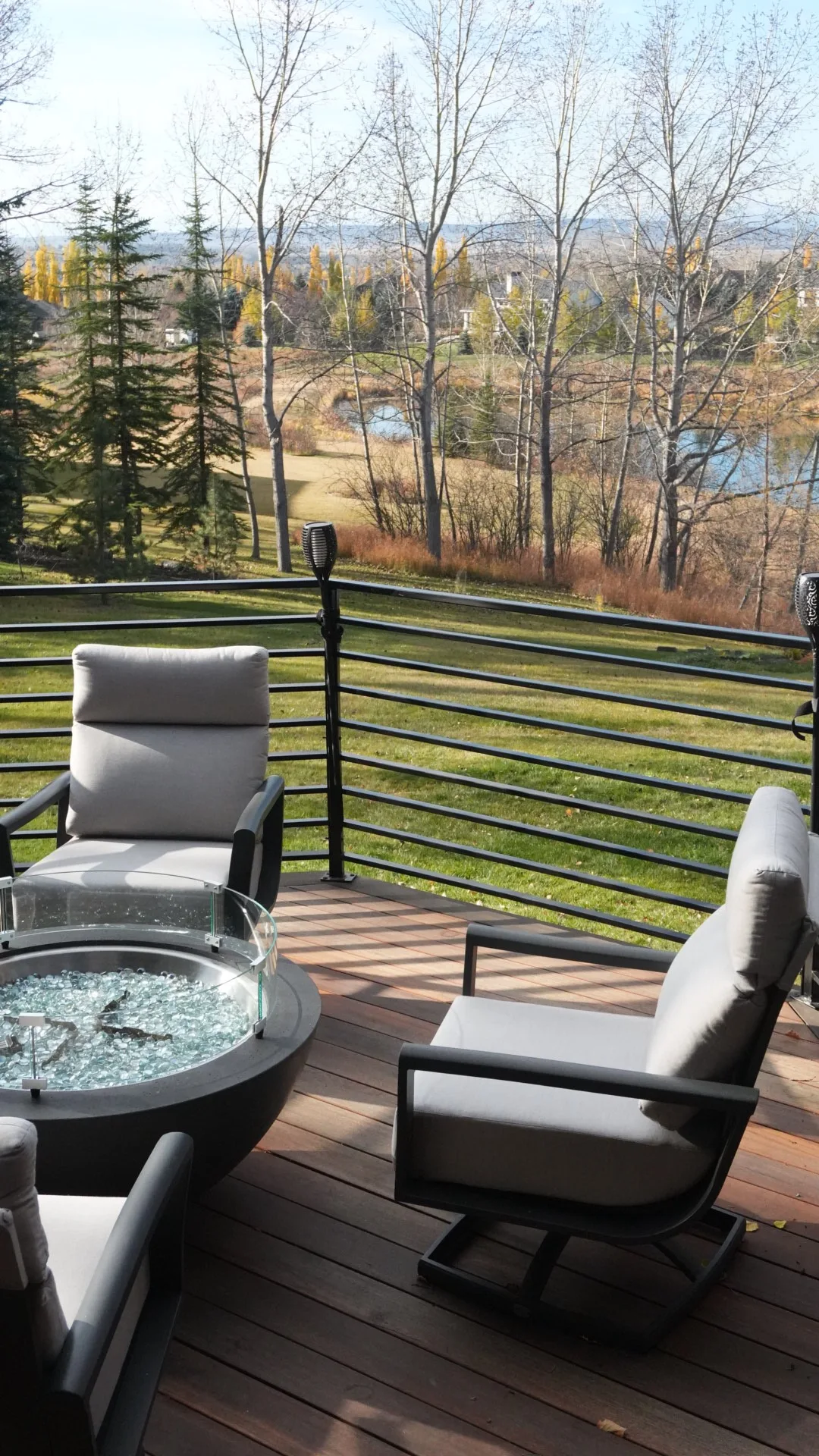 Deck fire table with a glass wind guard and horizontal railing overlooking a golf course in Calgary, AB