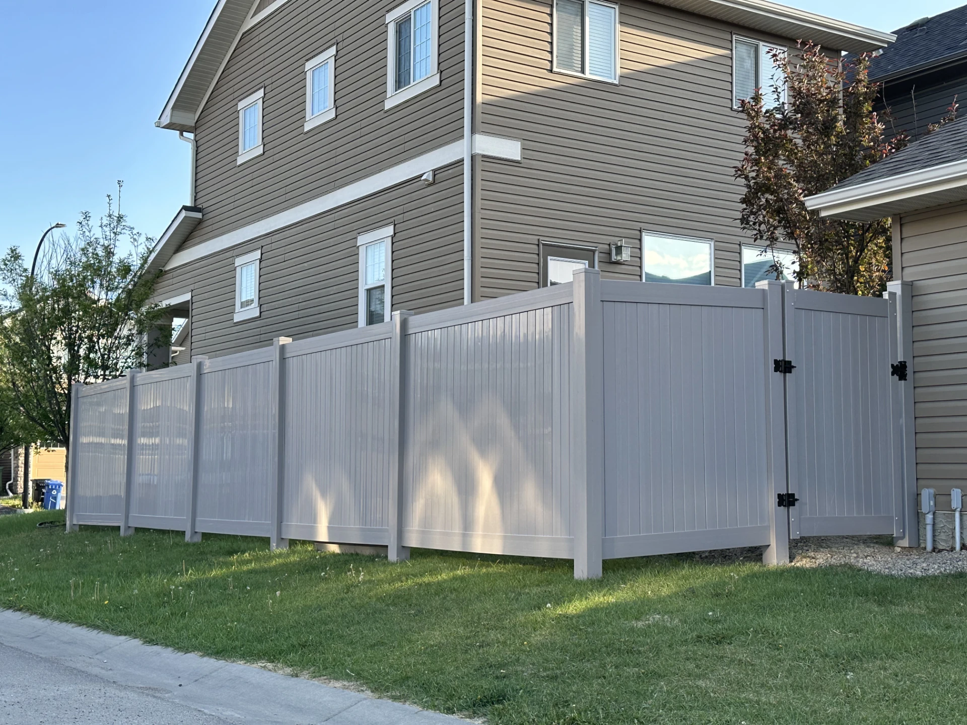 Front view of long white vinyl privacy fence with side gate next to a house above a little on the grass