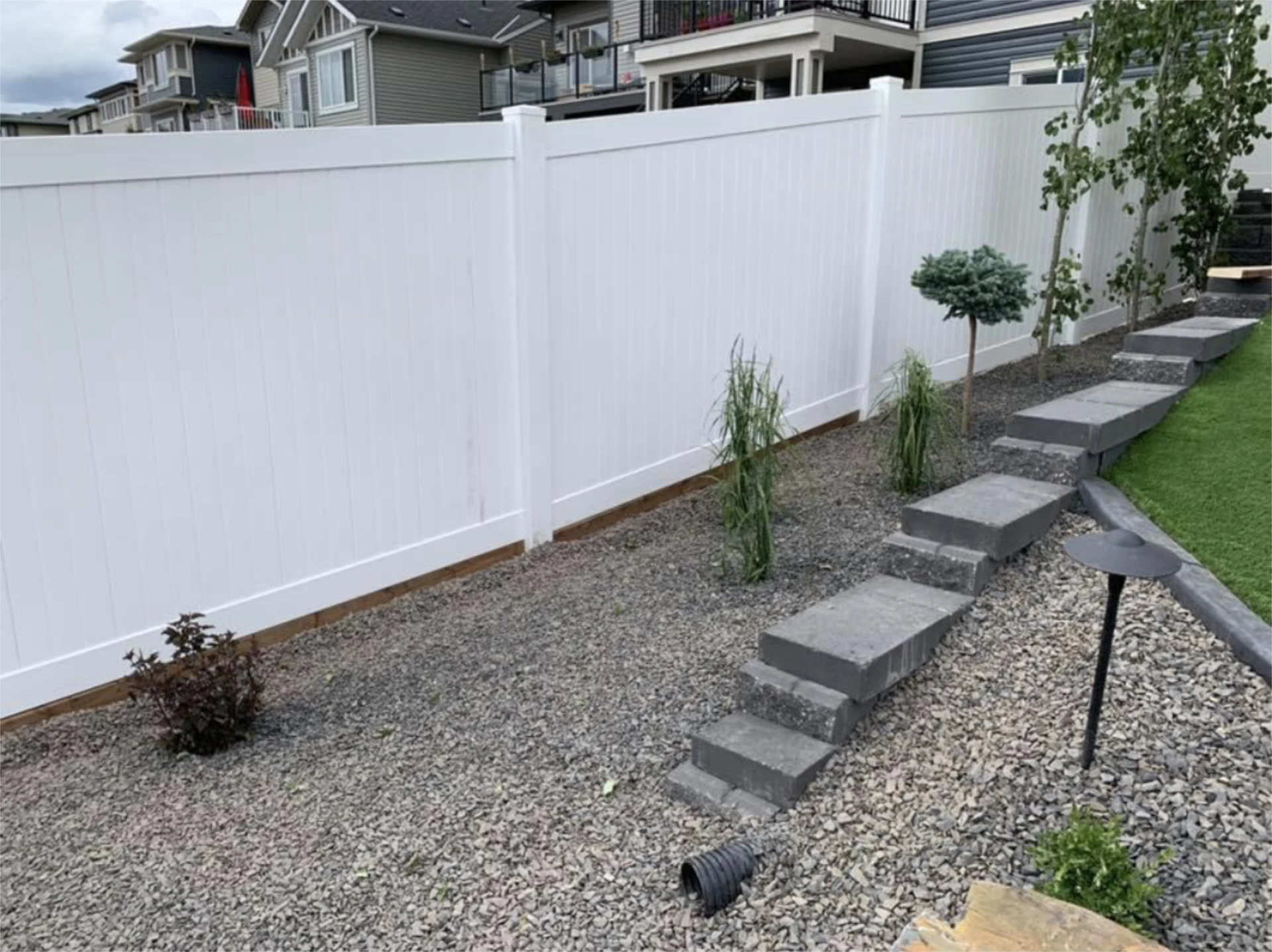 Landscaped yard with white privacy wide fence and plants beside the fence