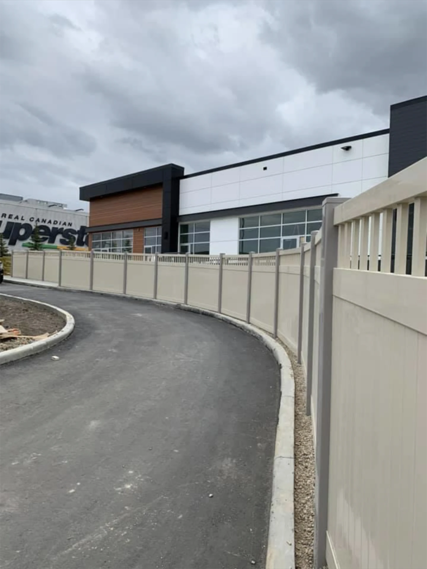 Long beige vinyl privacy fence along commercial driveway with cloudy weather