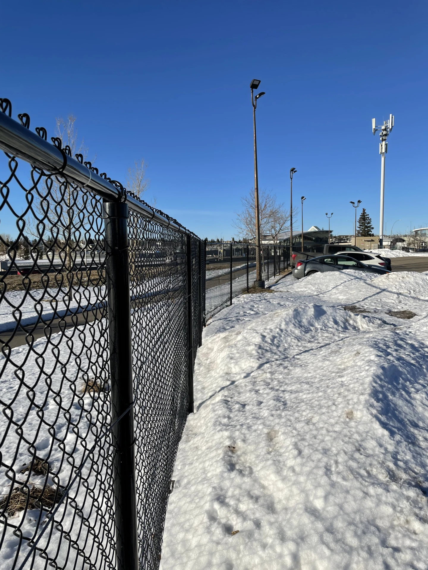 Long chain link fence beside snowy parking area with blue sky