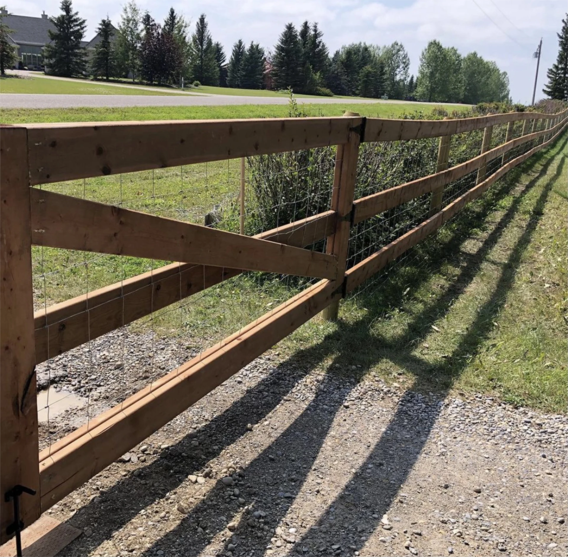 Long rustic wood and wire ranch fence along roadside with plants beside