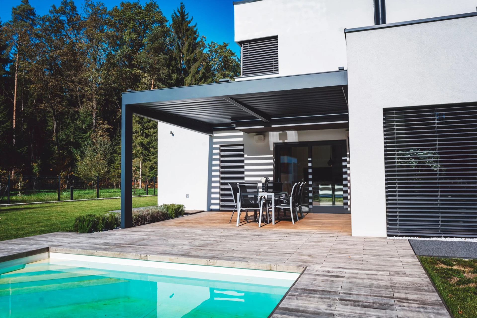 Modern house with patio and swimming pool with black sunroof pergola and forest view on the side of the house