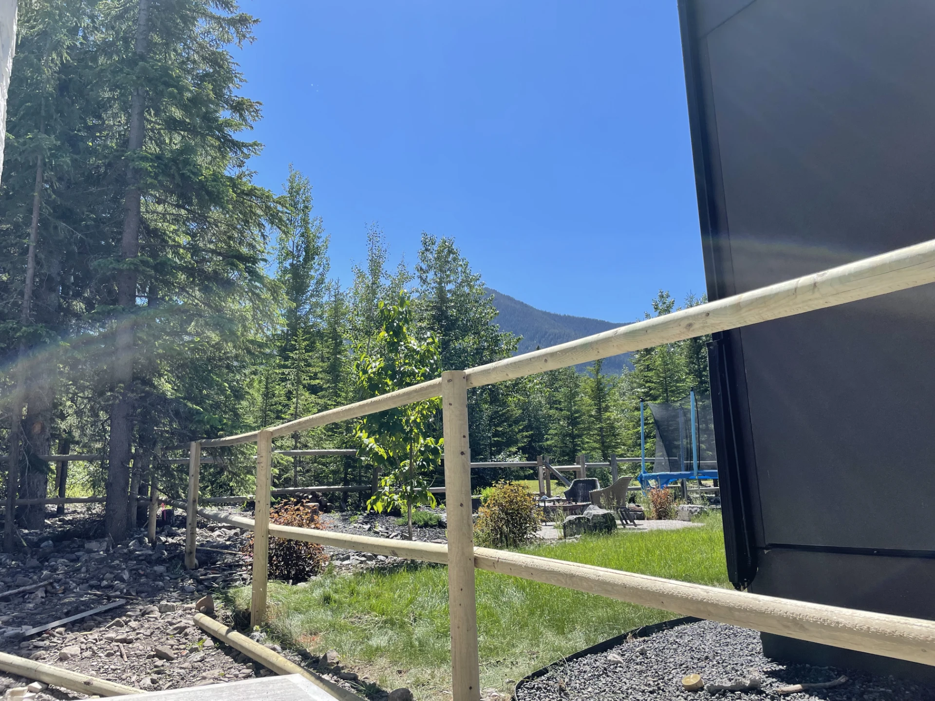Modern wooden rail fence beside forested mountain property with sky clear view