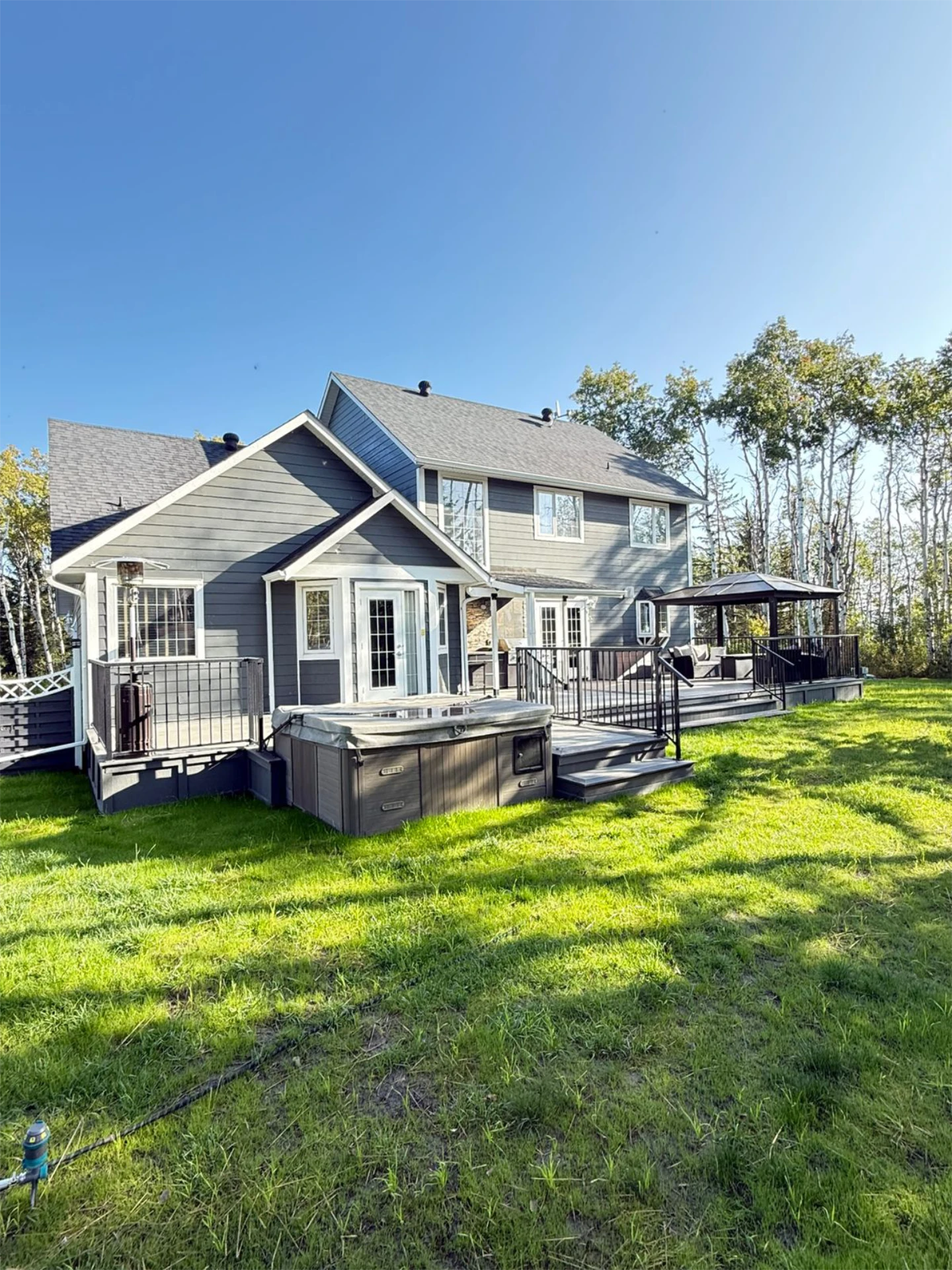 Multi level backyard deck with black railing hot tub and gazebo behind a gray house and overlooking view