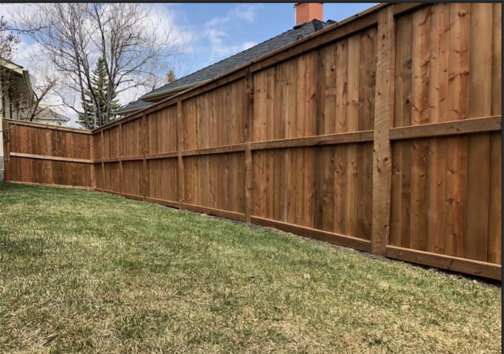 Wooden privacy fence installation along backyard lawn